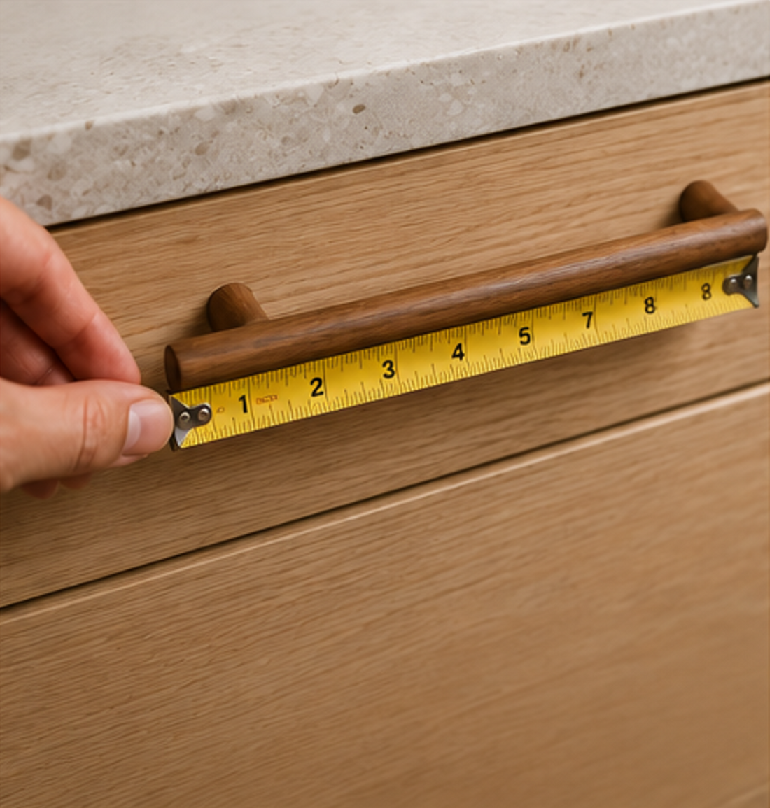 Measuring the center-to-center distance of a wooden cabinet handle using a tape measure for accurate hardware selection.