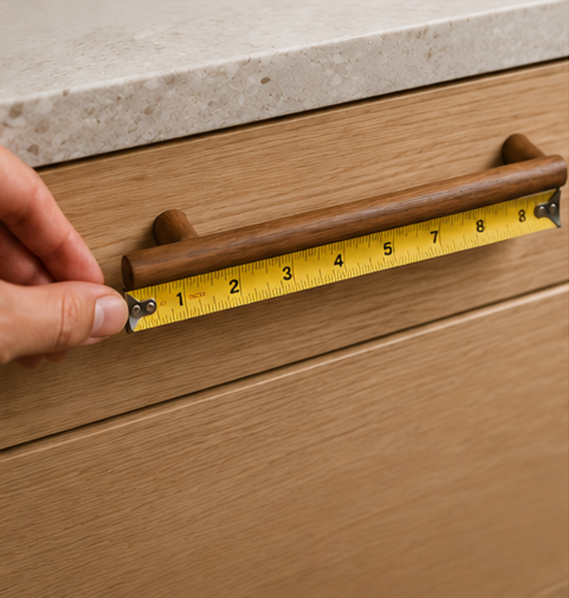 Measuring the center-to-center distance of a wooden cabinet handle using a tape measure for accurate hardware selection.